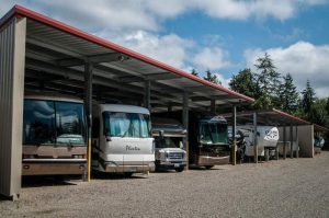 A row of recreational vehicles parked under a covered storage area with a clear sky in the background.