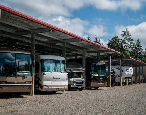 A row of recreational vehicles parked under a covered storage area with a clear sky in the background.